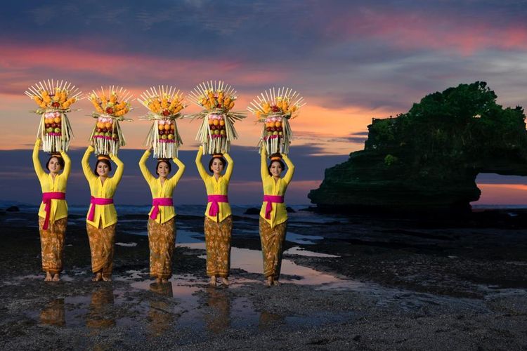 Balinese girls in traditional costume place offerings on their head