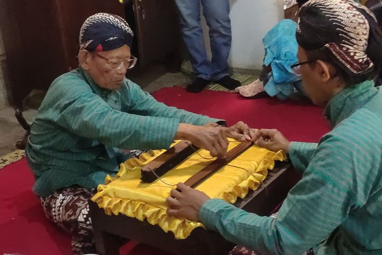 Mbah Sukaryono (78) memandikan kitab Kalimasadandi rumah mereka pada Pedukuhan Klebakan, Kalurahan Salamrejo, KapanewonnSentolo, Kabupaten Kulon Progo, Daerah Istimewa Yogyakarta. Anggota keluarga besar dan mereka yang diundang bergantian memandikan tiap lembar kitab.