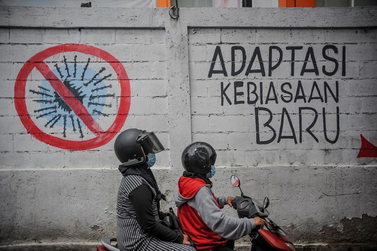 Pengendara sepeda motor melintas di depan mural Adaptasi Kebiasaan Baru?, di perbatasan antara Babakan Surabaya dengan Antapani di Bandung, Jawa Barat, Rabu (3/2/2021).