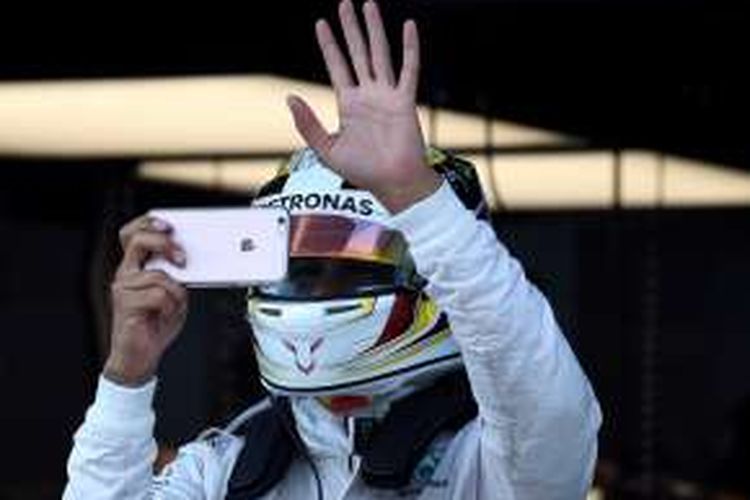 Pebalap Mercedes asal Inggris, Lewis Hamilton, melambai kepada penonton sambil mengambil foto dengan telepon genggamnya saat sesi latihan kedua GP Malaysia di Sirkuit Sepang, Jumat (30/9/2016).