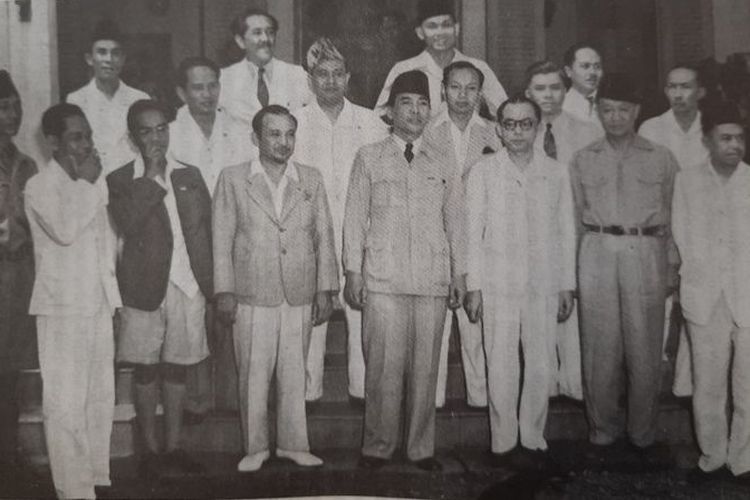 Menteri Penerangan Amir Sjarifuddin (depan, nomor dua dari kiri, mengenakan jas dan bercelana pendek), bersama Presiden Sukarno, Wapres Mohammad Hatta, dan menteri-menteri kabinet pertama, 4 Oktober 1945.