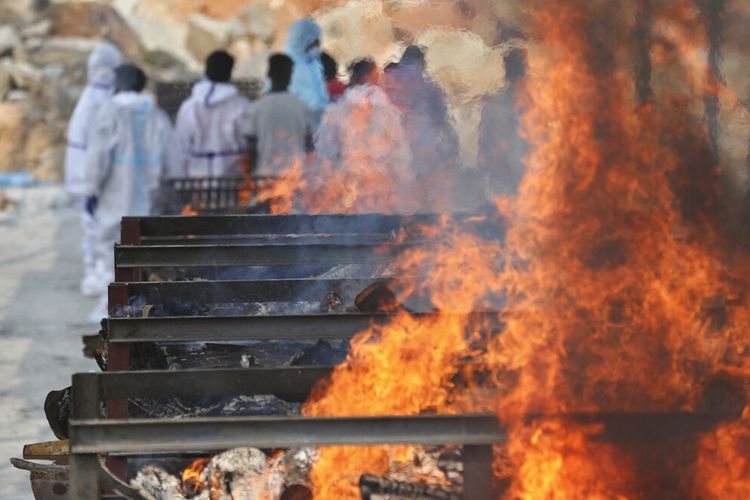 Family members perform last rites of a person who died of COVID-19 as funeral pyres of other victims burn at an open crematorium set up at a granite quarry on the outskirts of Bengaluru, India, Wednesday, May 5, 2021. (AP Photo/Aijaz Rahi)