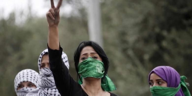 Perempuan Palestina, dengan menutup mulut menggunakan syah Hamas, emngacungkan tanda victory saat bentrokan dengan tentara Israel di Beit El, dekat ramalla, Tepi Barat, 10 Oktober 2015.