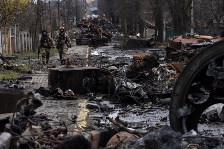 Sejumlah tentara Ukraina berjalan di tengah puing-puing tank milik pasukan Rusia yang hancur di Bucha, wilayah pinggiran Kyiv, pada pada 3 April 2022. 
