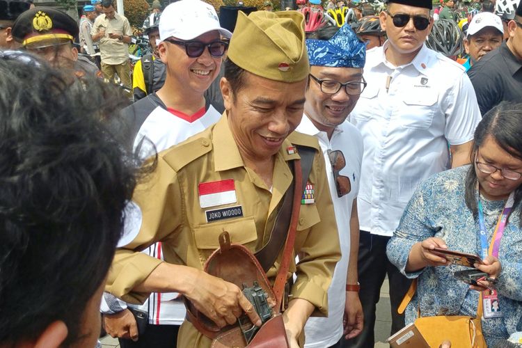Presiden Joko Widodo mengenakan pakaian ala Bung Tomo saat bersepeda di depan Gedung Sate yang juga kantor Gubernur Jawa Barat, Sabtu (10/11/2018) pagi. Jokowi lalu memamerkan pistol mainan yang disimpan ditasnya.