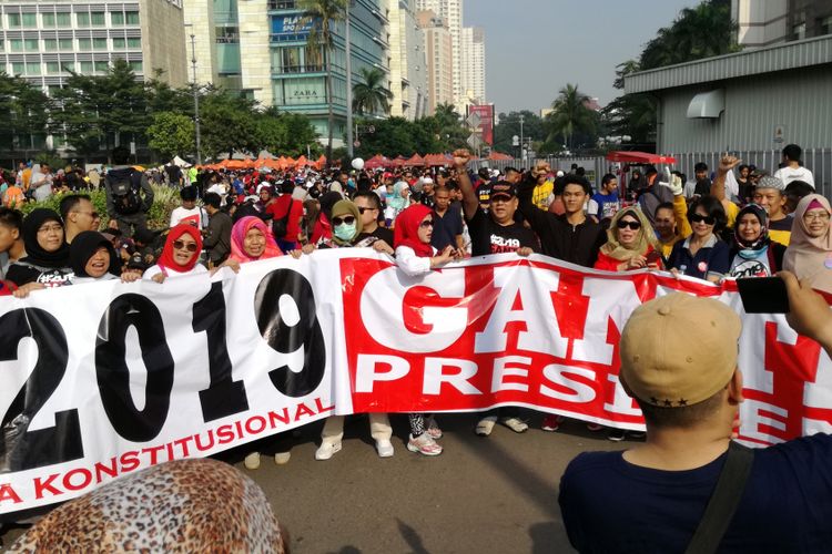 Sejumlah warga tampak berjalan kaki dengan spanduk sembari memakai kaus dan kaus #2019GantiPresiden di Bundaran HI, Jakarta, Minggu (29/4/2018).