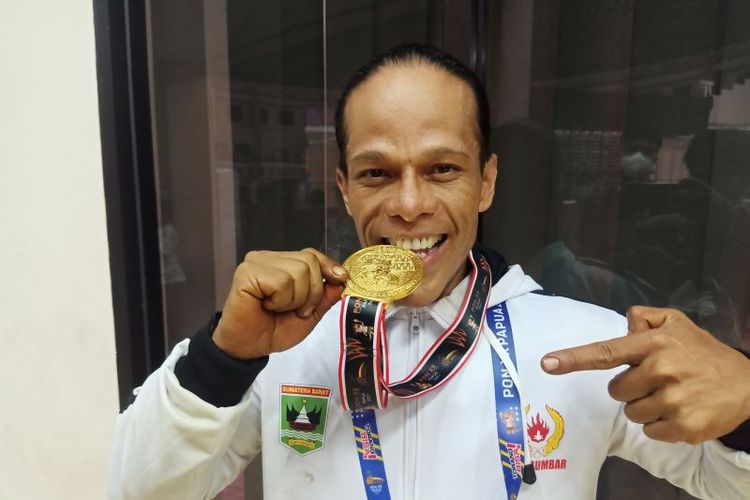 Atlet binaraga asal Sumatera Barat Muswar alias Iwan Samuray menggigit medali emas PON XX Papua dari nomor 75 Kg di Auditorium Uncen, Kabupaten Jayapura, Papua, Senin (4/10/2021). 