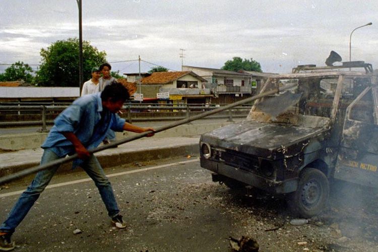 Seorang Pria memukul mobil yang rusak terbakar di Jakarta dalam tregedi Mei 1998.