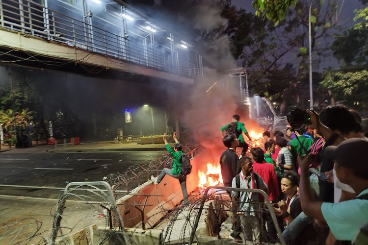 Spanduk dibakar di depan pembatas beton saat kericuhan demo mahasiswa di Jalan Medan Merdeka Barat, Gambir, Jakarta Pusat, Jumat (20/10/2023). (KOMPAS.com/XENA OLIVIA)