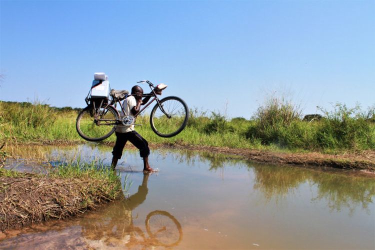 Sebuah estafet komunitas melintasi aliran air dengan sepedanya untuk memvaksinasi anak-anak di zona kesehatan Manono, Provinsi Tanganyika, di Republik Demokratik Kongo pada tahun 2018