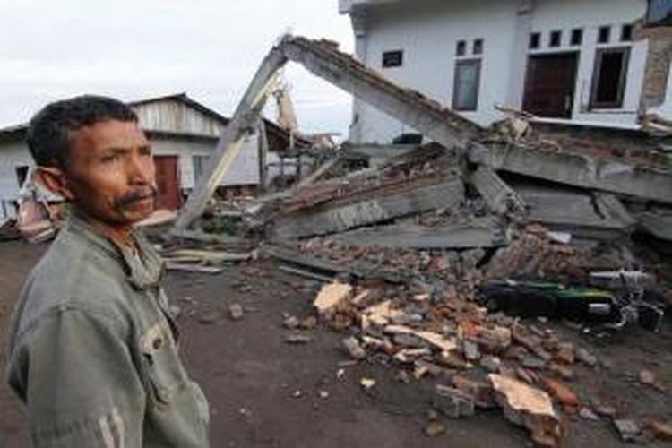 Warga berdiri di depan bangunan yang hancur diguncang gempa di Blang Mancung, Aceh, 3 Juli 2013. Gempa berkekuatan 6.2 SR yang terjadi 2 Juli di Aceh, menghancurkan rumah dan mengakibatkan tanah longsor. 24 orang tewas dan ratusan terluka.