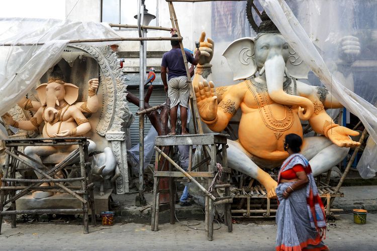 Seorang wanita berjalan melewati seorang pengrajin yang sedang mengerjakan patung dewa Hindu berkepala gajah Ganesha di sebuah studio pinggir jalan di Kolkata, India, Rabu, 8 September 2021.
