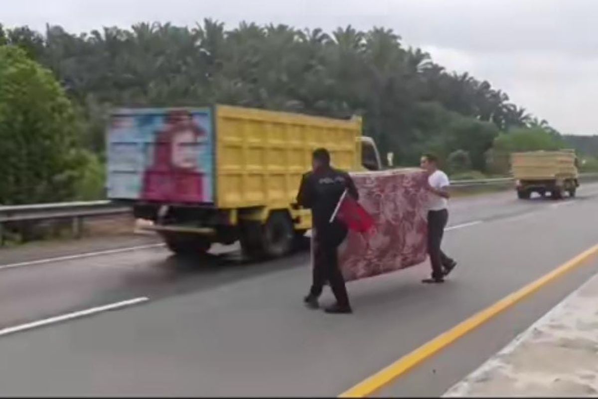 Kasur sedang dipungut oleh petugas kepolisian setelah terhempas di jalan tol