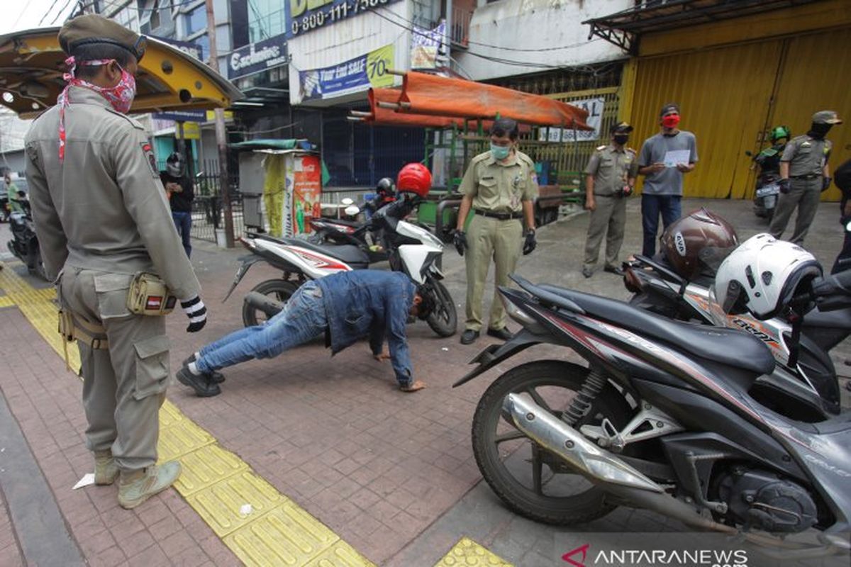 Petugas gabungan memberikan hukuman push up kepada warga yang tidak memakai masker saat razia penerapan aturan Pembatasan Sosial Berskala Besar (PSBB) di Kawasan Jalan Fatmawati, Jakarta, Selasa (28/4/2020). ANTARA FOTO/Reno Esnir/pras. 