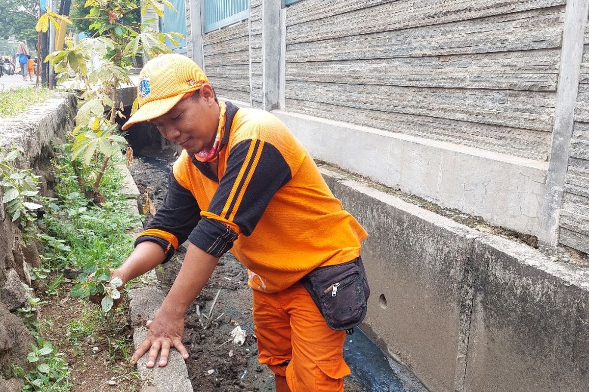 Robbi Firli Adi (28) anggota PPSU Kedoya Utara, Kebon Jeruk, Jakarta Barat, tengah memebersihkan saluran air di Jalan Daan Mogot, Jakarta Barat.