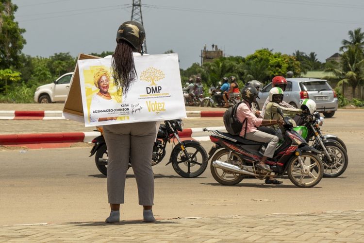 Seorang wanita berdiri di pinggir jalan membawa spanduk kampanye Pemilu di Togo pada 24 April 2024.