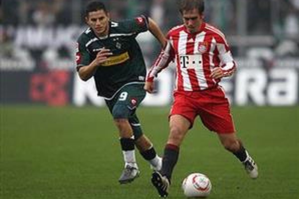 Defender Bayern Muenchen, Philipp Lahm, dibayangi pemain Borussia Moenchengladbach. Lahm akhirnya mencetak gol dan menyelamatkan timnya dari kekalahan.