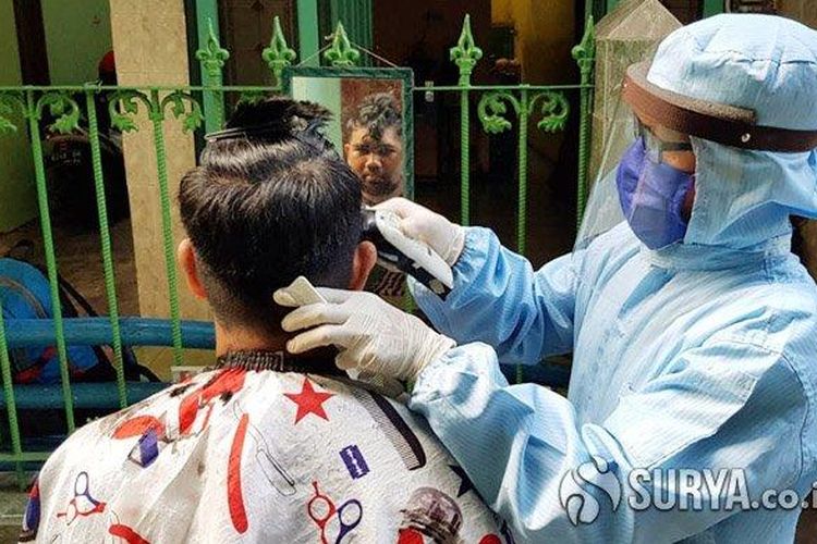 Suyadi (49) seorang tukang cukur rambut keliling saat melayani pelanggan menggunakan Alat Pelindung Diri (APD) lengkap layaknya tenaga medis di Surabaya, Jumat (8/5/2020). 