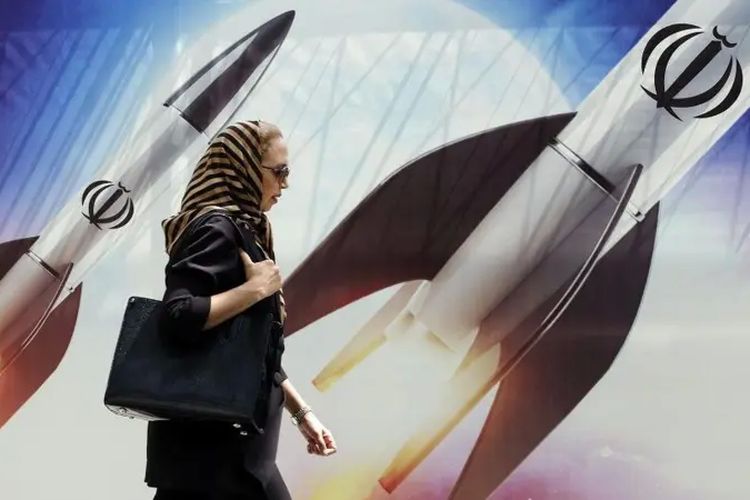 Seorang perempuan berjalan melintasi spanduk bergambar rudal Iran di Teheran, Selasa (16/4/2024).