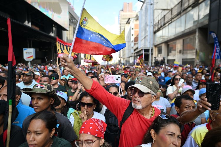 Seorang pendukung Presiden Venezuela yang digulingkan, Nicolas Maduro, mengibarkan bendera Venezuela selama demonstrasi untuk menonton sidang Majelis Nasional di layar besar di Caracas pada 5 Januari 2026. Parlemen baru Venezuela dibuka pada 5 Januari dengan para anggota parlemen berteriak ?Ayo Nico!? saat mereka secara paksa mengecam penangkapan pemimpin kiri Nicolas Maduro dalam operasi militer AS pada 3 Januari.