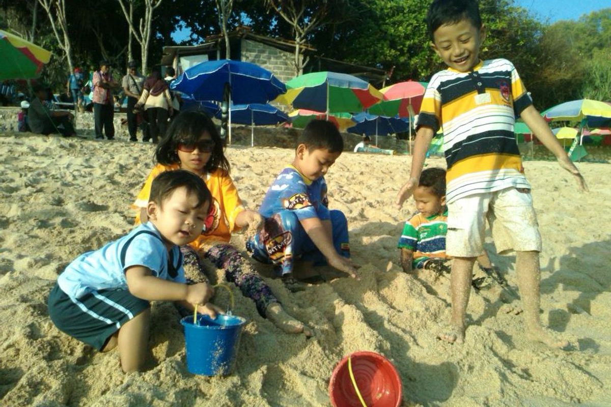 Anak bermain pasir di pantai sambil belajar.