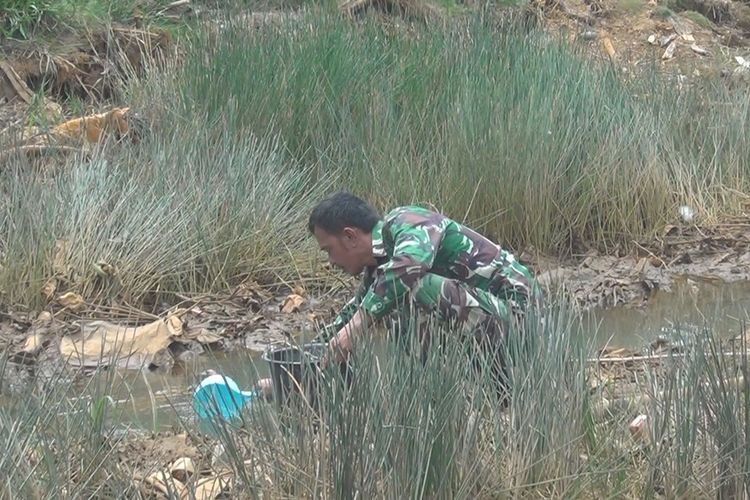 Seorang anggota TNI yang bertugas sebagai Babinsa di  Desa Arisan Jaya Ogan Ilir membantu mengambil air dari :Parit Cacing untuk warga yang kesulitan air, Rabu (2/10/2019). 