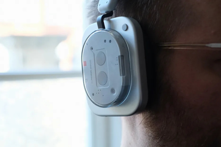 Tampilan ear-cup Headphone 1 Nothing. Bagian ini didesain oval dengan elemen transparan, menampilkan komponen internal perangkat berupa dua logam kecil yang berfungsi sebagai ruang akustik perangkat. 
