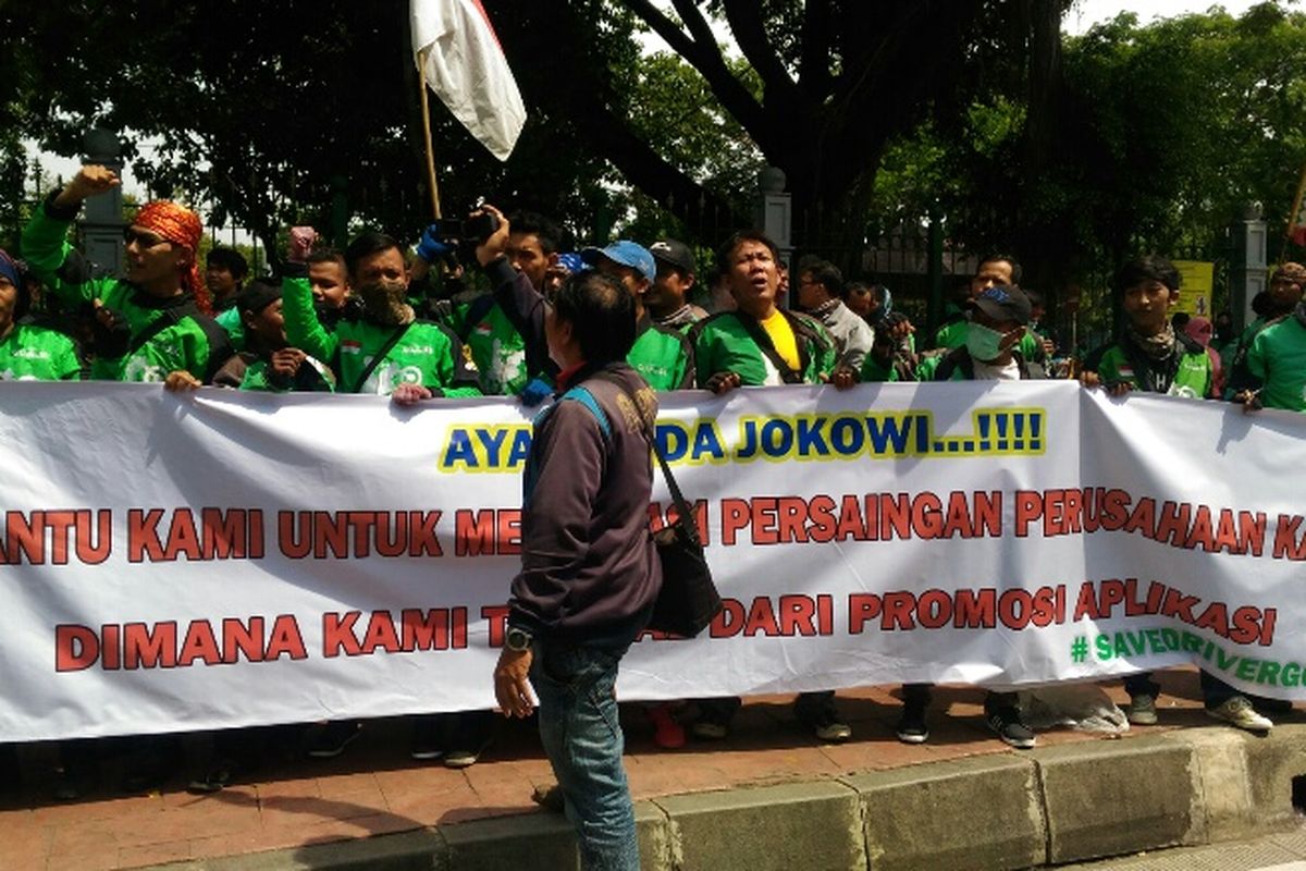 Massa ojek online membentangkan spanduk di Lapangan IRTI sebelum long march ke Kemenhub dan Istana Negara, Kamis (23/11/2017).