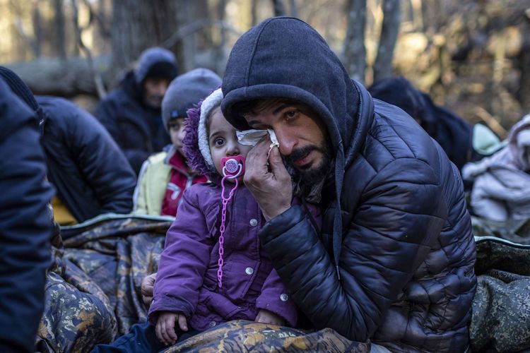 Seorang pria migran yang menggendong anak menangis di perbatasan dekat Narewka, Polandia, sekitar perbatasan Polandia-Belarus, Selasa (9/11/2021). Polandia dan negara-negara Uni Eropa (UE) menuduh Belarus mendorong para migran untuk secara ilegal melintasi perbatasan sebagai pembalasan atas sanksi yang dijatuhkan UE kepada Minsk atas pelanggaran HAM.