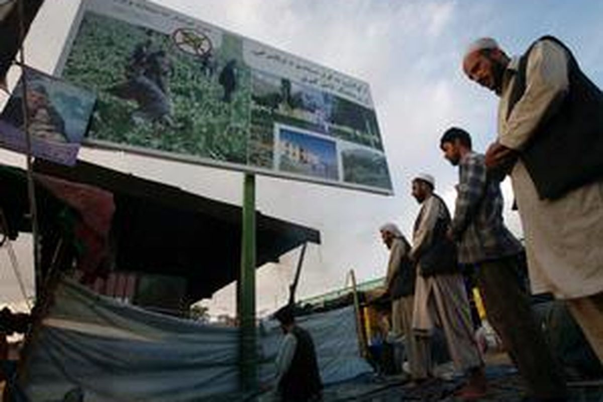 Warga Afganistan sembahyang di samping sebuah papan reklame yang berisi seruan menentang tumbuhnya opium di Kabul, Afganistan, Rabu, 2 September 2009.  