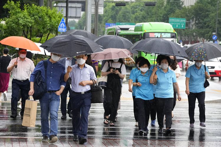 Orang-orang yang memakai masker wajah sebagai tindakan pencegahan terhadap virus corona berjalan di tengah hujan di jalan di Seoul, Korea Selatan, Rabu, 30 Juni 2021.