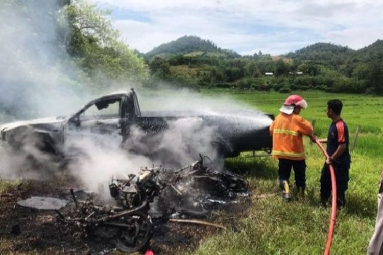 Pemadam kebakaran menyemprotkan air ke mobil pick up yang dibakar massa