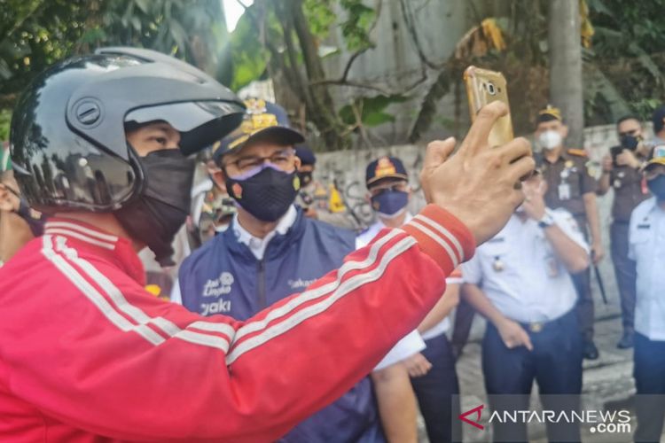 Gubernur DKI Jakarta Anies Baswedan (kanan) swafoto bersama pengendara di pos penyekatan PPKM Darurat kawasan Daan Mogot, Jakarta Barat, Rabu (7/7/2021). 