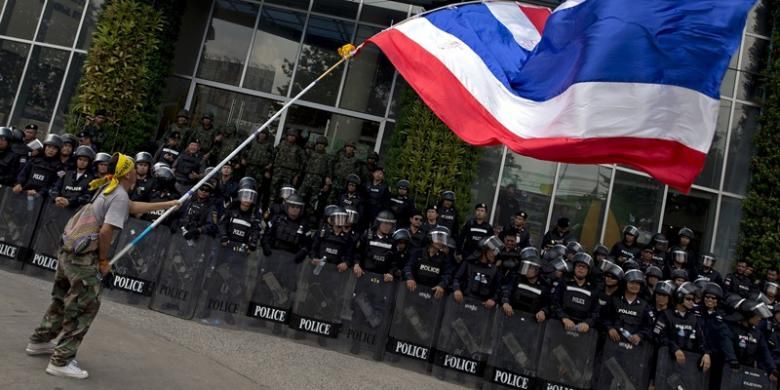 Seorang pengunjuk rasa anti-pemerintah mengibarkan bendera Thailand di depan barikade polisi yang menjaga sebuah stasiun televisi di Bangkok, Jumat (9/5/2014).