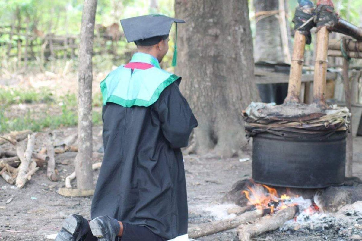 Jon, saat mengenakan pakaian wisuda lengkap dengan toga, berlutut di depan tempat penyulingan sopi