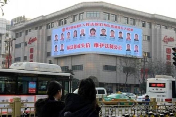 Sebuah papan reklame yang terpasang di salah satu gedung di jalanan kota Xian, China memajang foto warga yang tidak membayar utang.