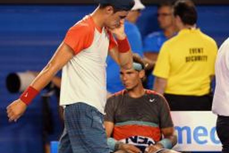 Petenis Australia, Bernard Tomic (depan) melangkah melewati petenis Spanyol, Rafael Nadal, untuk menjalani perawatan medis, saat keduanya bertemu di babak pertama Australian Open di Melbourne Parks, Selasa (14/01/2014).