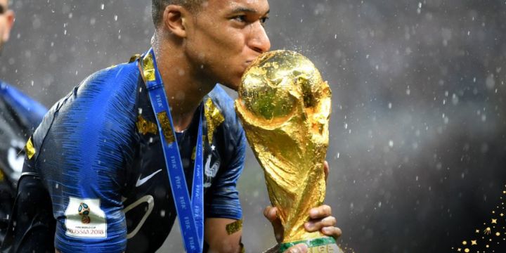 Penyerang muda Perancis, Kylian Mbappe, saat berselebrasi mencium trofi Piala Dunia 2018 di tengah cuaca hujan.