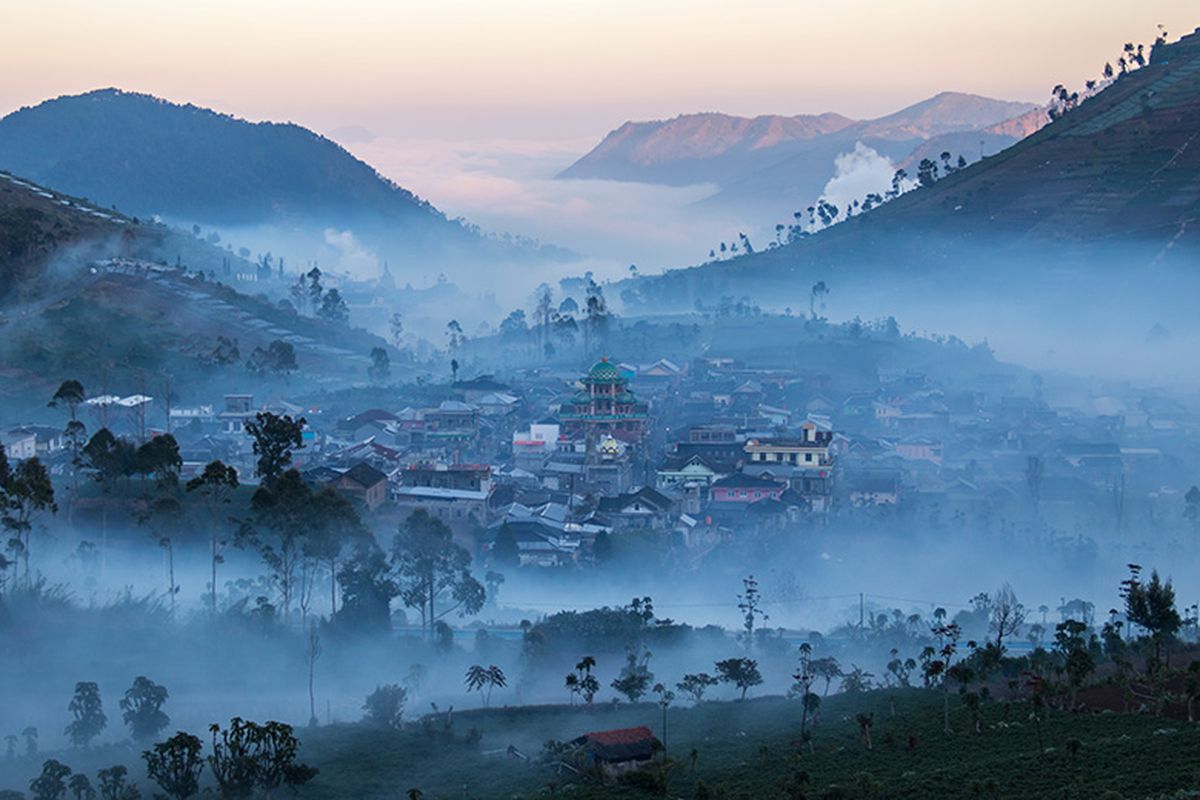 Kawasan Dieng berkabut — perbukitan hijau dan lembah yang diselimuti kabut tipis pagi hari, terlihat dari ketinggian