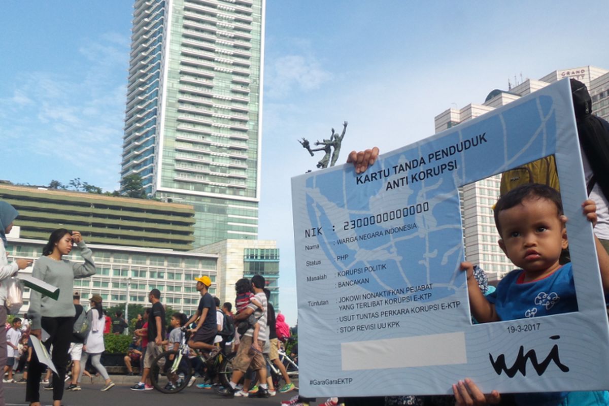 Seorang balita tengah berpose dengan menggunakan alat peraga bertuliskan “KTP Anti Korupsi” saat kegiatan car free day di Bundaran Hotel Indonesia, Minggu (19/3/2017). Sejumlah kelompok masyarakat menyerukan gerakan agar pemerintah serius mengusut kasus dugaan korupsi e-KTP hingga tuntas.