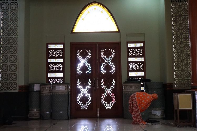 Seorang perempuan menunaikan salat di dekat pintu kayu berukir gaya Jepara di Masjid Agung Al-Barkah, Kota Bekasi.