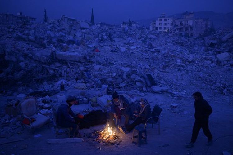 Penduduk setempat menunggu kabar dari kerabat mereka, duduk di dekat api unggun di antara puing-puing bangunan yang runtuh di Hatay, Turkiye pada Selasa (14/2/2023), setelah gempa berkekuatan magnitudo 7,8 melanda tenggara negara itu. Pada Jumat (17/2/2023), tujuh orang sekeluarga asal Suriah dilaporkan meninggal dunia akibat kebakaran di Turkiye pada Jumat (17/2/2023).