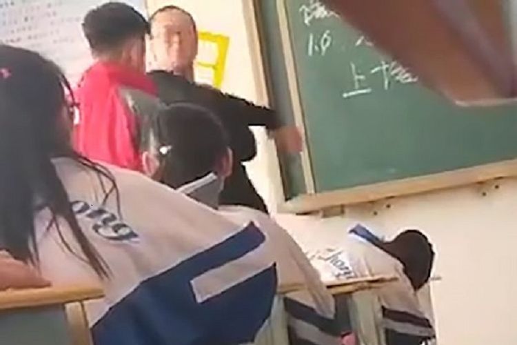 Dalam foto yang diambil dari rekaman video ini terlihat sang guru menampar seorang murid laki-laki di depan kelas.