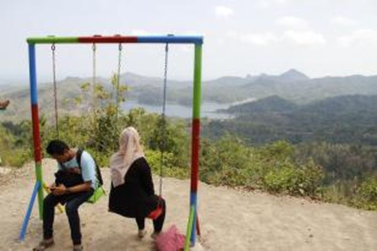 Dua wisatawan duduk di atas ayunan baru  di obyek wisata alam Kalibiru, Kulon Progo, Daerah Istimewa Yogyakarta, Sabtu (22/8/2015). Dari spot foto ayunan ini, wisatawan juga dapat melihat pemandangan Waduk Sermo dan Pegunungan Menoreh.