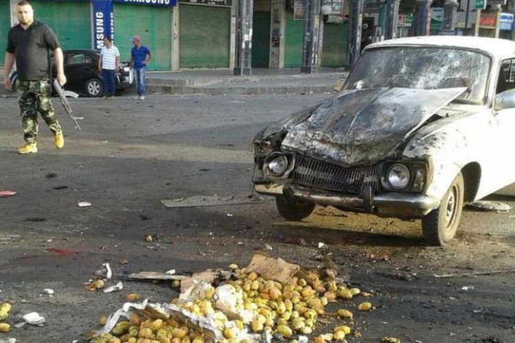 Seorang anggota pasukan keamanan Suriah berjalan melewati sebuah truk yang rusak akibat serangan bunuh diri di kota Sweida di Suriah, Rabu (25/7/2018). (AFP/SANA)