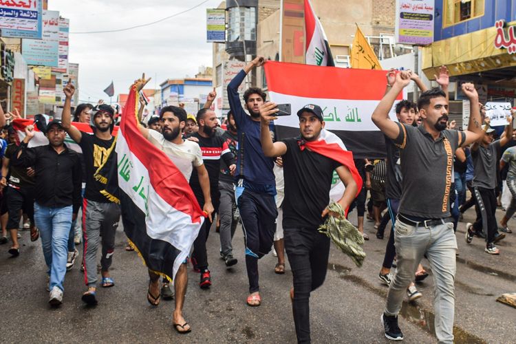 Para demonstran Irak berlari membawa bendera nasional dalam demonstrasi menentang pemerintah yang terjadi di Nasiriyah, ibu kota Provinsi Dhi Qar, pada 25 Oktober 2019.