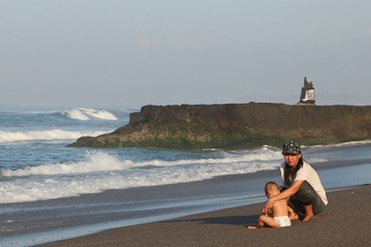 Pengunjung Pantai Batu Bolong yang membawa anaknya bermain ombak di tepi pantai batu bolong, Canggu