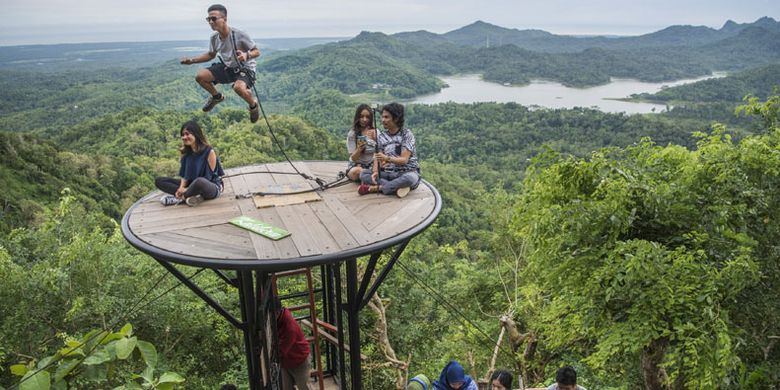 Wisatawan menunggu giliran berfoto dengan latar belakang pemandangan Waduk Sermo di obyek wisata Kalibiru, Desa Hargowilis, Kecamatan Kokap, Kulon Progo, DI Yogyakarta, Jumat (2/12/2016). Obyek wisata itu dikembangkan dan dikelola warga setempat sehingga mampu menjadi sumber pendapatan bagi masyarakat di kawasan itu. 