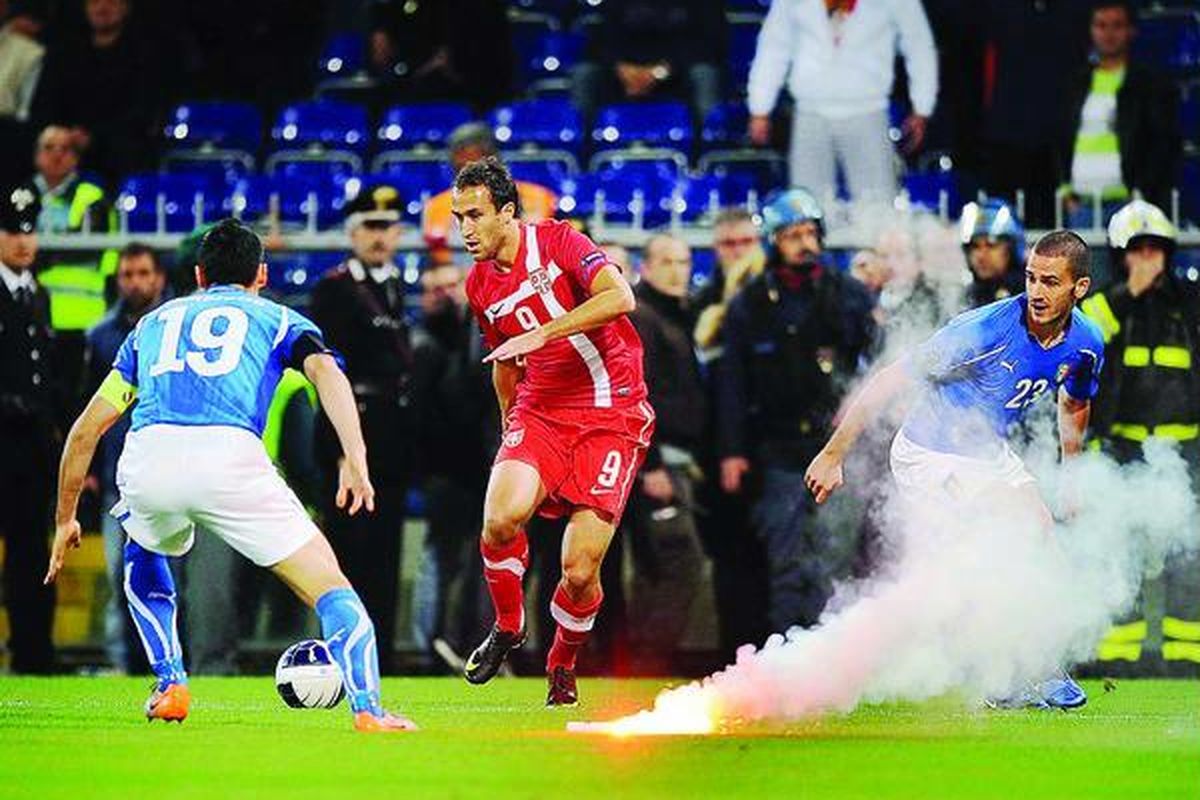 Sebuah api suar dilontarkan suporter Serbia saat pemain Italia, Gianluca Zambrotta (kiri) dan Leonardo Bonucci (kanan), tengah berlaga dengan pemain Serbia, Dragan Mrdja, pada pertandingan Grup C penyisihan Euro 2012 di Stadion Luigi Ferraris, Genoa, Italia, Selasa (12/10). Pertandingan yang rusuh itu dihentikan dengan ke- dudukan 0-0.
