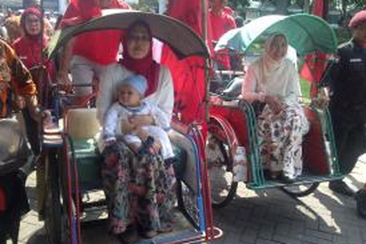 Pasangan calon Bupati dan Wakil Bupati Malang, Dewanti-Masrifah (kiri-kanan) naik becak dengan membawa bayi saat akan mendaftar ke KPU Kabupaten Malang. Senin (27/7/2015).